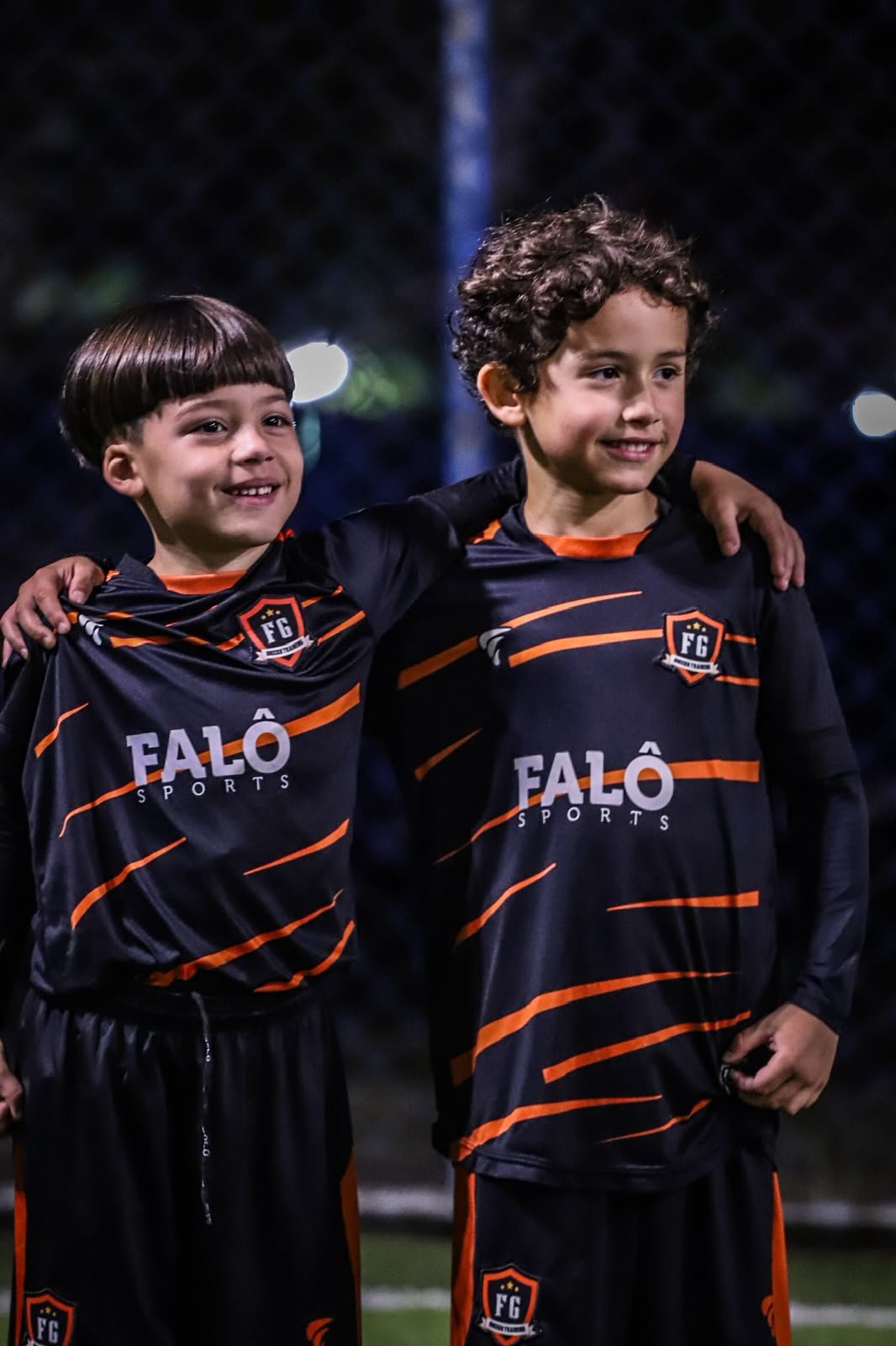 Atletas de base com o uniforme preto e laranja da FG Soccer Training