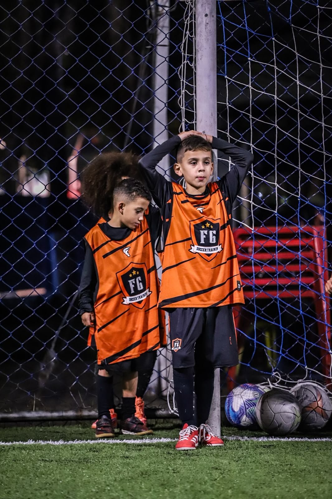 Dois atletas com colete laranja da FG apoiados na trave ao lado das bolas de treino