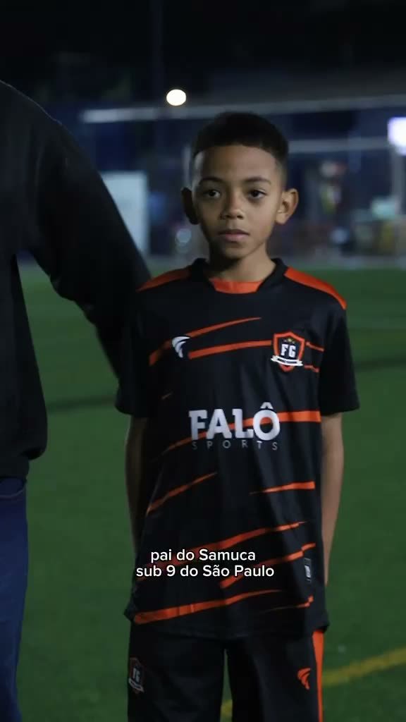 Atleta da FG Soccer Training com o uniforme preto e laranja ao lado do pai, em campo à noite